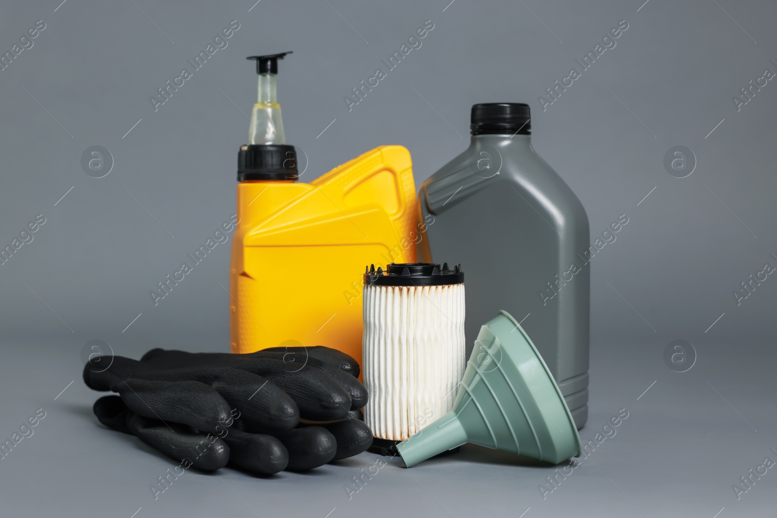 Motor oil in plastic canisters, filter, gloves and funnel on grey background Photo of Motor oil in plastic canisters, filter, gloves and funnel on grey background