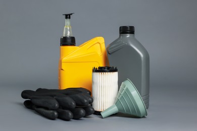 Photo of Motor oil in plastic canisters, filter, gloves and funnel on grey background