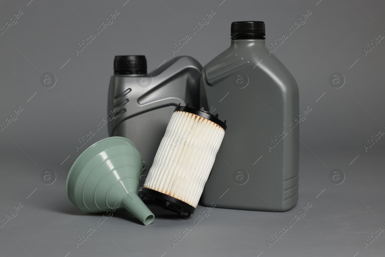 Motor oil in plastic canisters, filter and funnel on grey background Photo of Motor oil in plastic canisters, filter and funnel on grey background