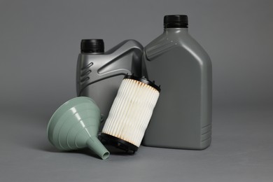 Photo of Motor oil in plastic canisters, filter and funnel on grey background