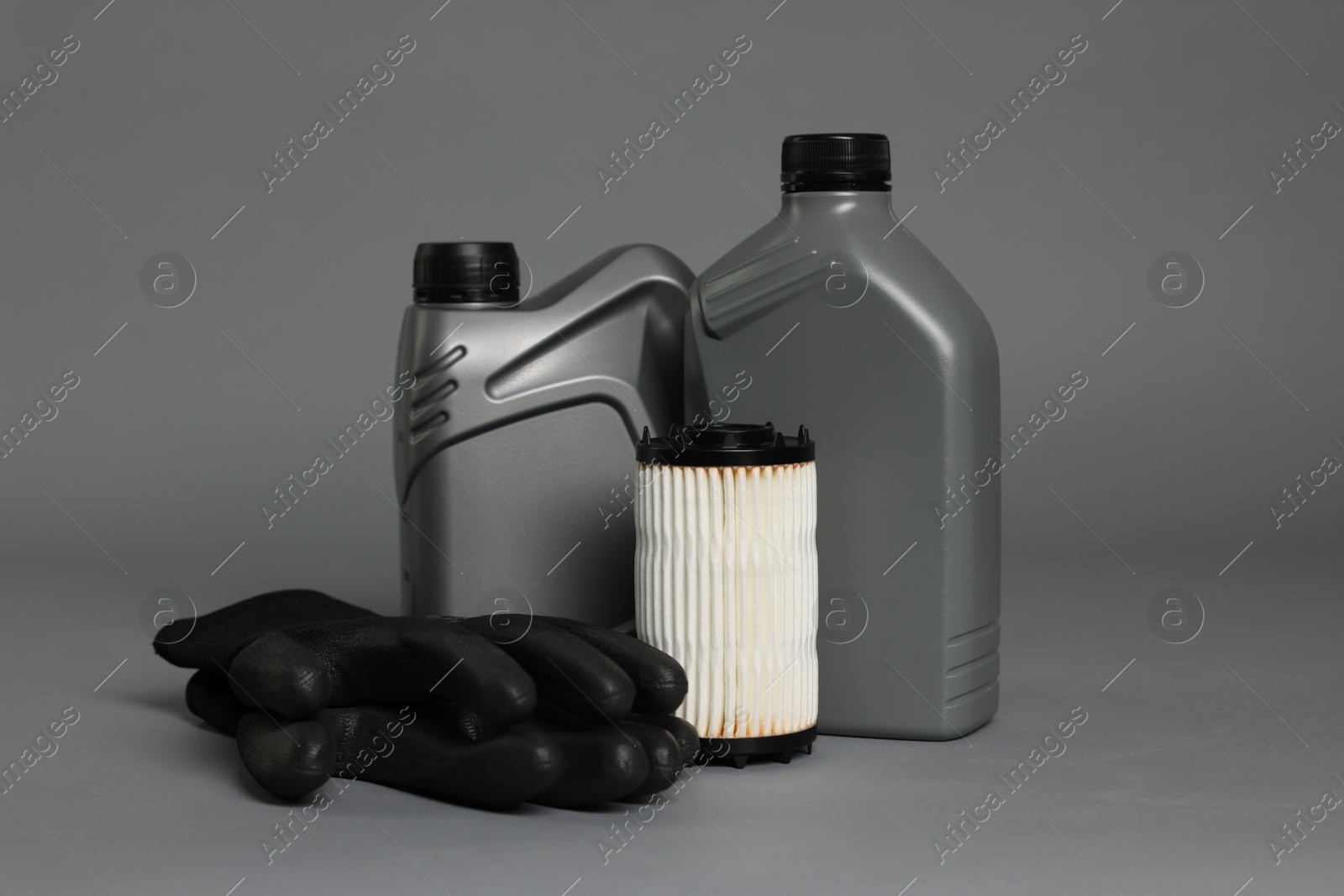 Motor oil in plastic canisters, gloves and filter on grey background Photo of Motor oil in plastic canisters, gloves and filter on grey background
