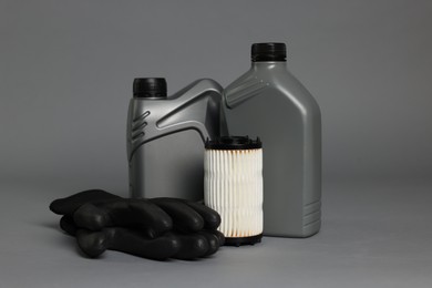 Photo of Motor oil in plastic canisters, gloves and filter on grey background