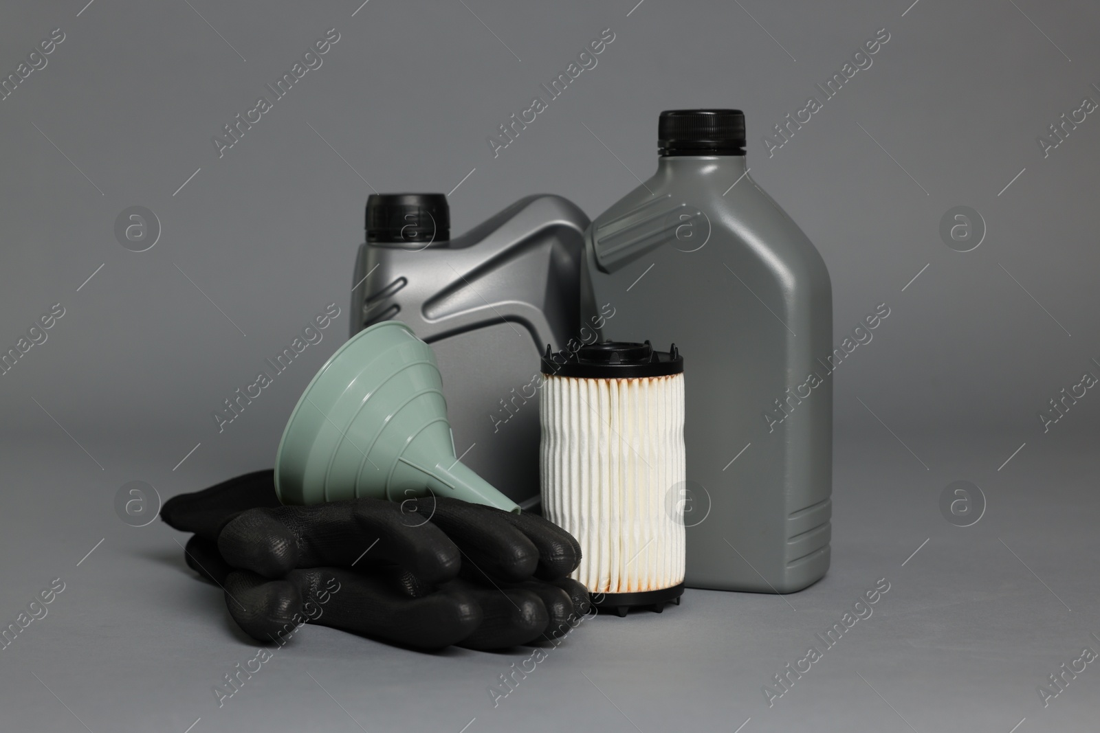 Motor oil in plastic canisters, filter, gloves and funnel on grey background Photo of Motor oil in plastic canisters, filter, gloves and funnel on grey background