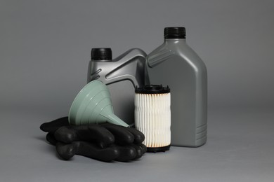 Photo of Motor oil in plastic canisters, filter, gloves and funnel on grey background