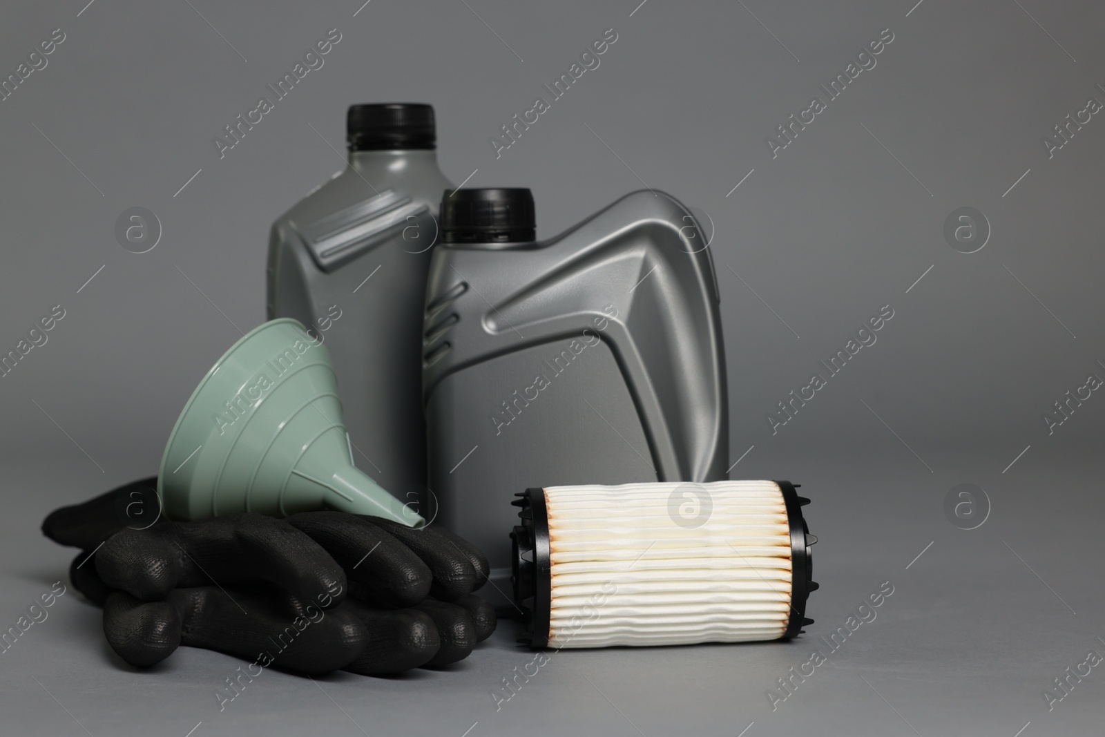 Motor oil in plastic canisters, filter, gloves and funnel on grey background Photo of Motor oil in plastic canisters, filter, gloves and funnel on grey background