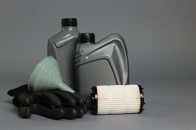 Photo of Motor oil in plastic canisters, filter, gloves and funnel on grey background