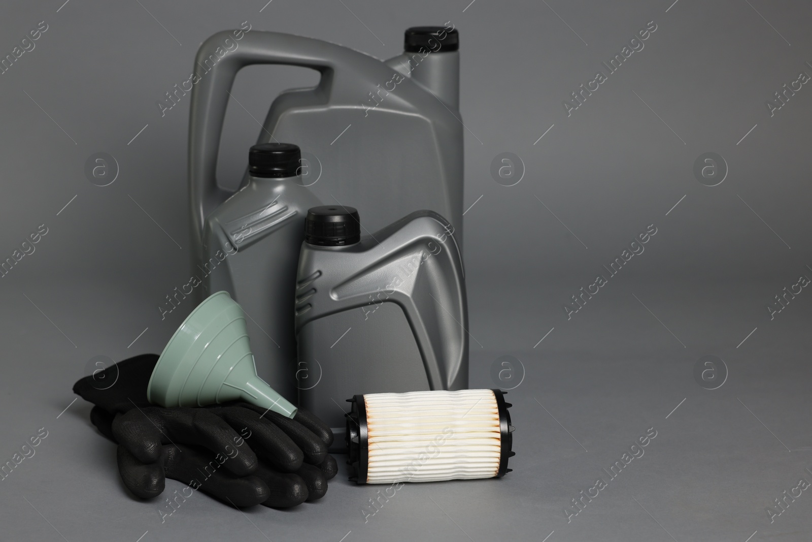 Motor oil in plastic canisters, filter, gloves and funnel on grey background, space for text Photo of Motor oil in plastic canisters, filter, gloves and funnel on grey background, space for text