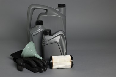 Photo of Motor oil in plastic canisters, filter, gloves and funnel on grey background, space for text