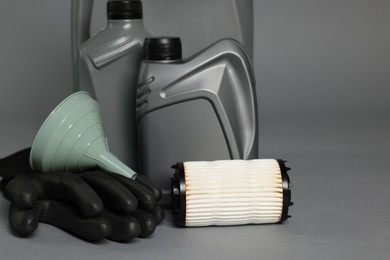 Photo of Motor oil in plastic canisters, filter, gloves and funnel on grey background, closeup