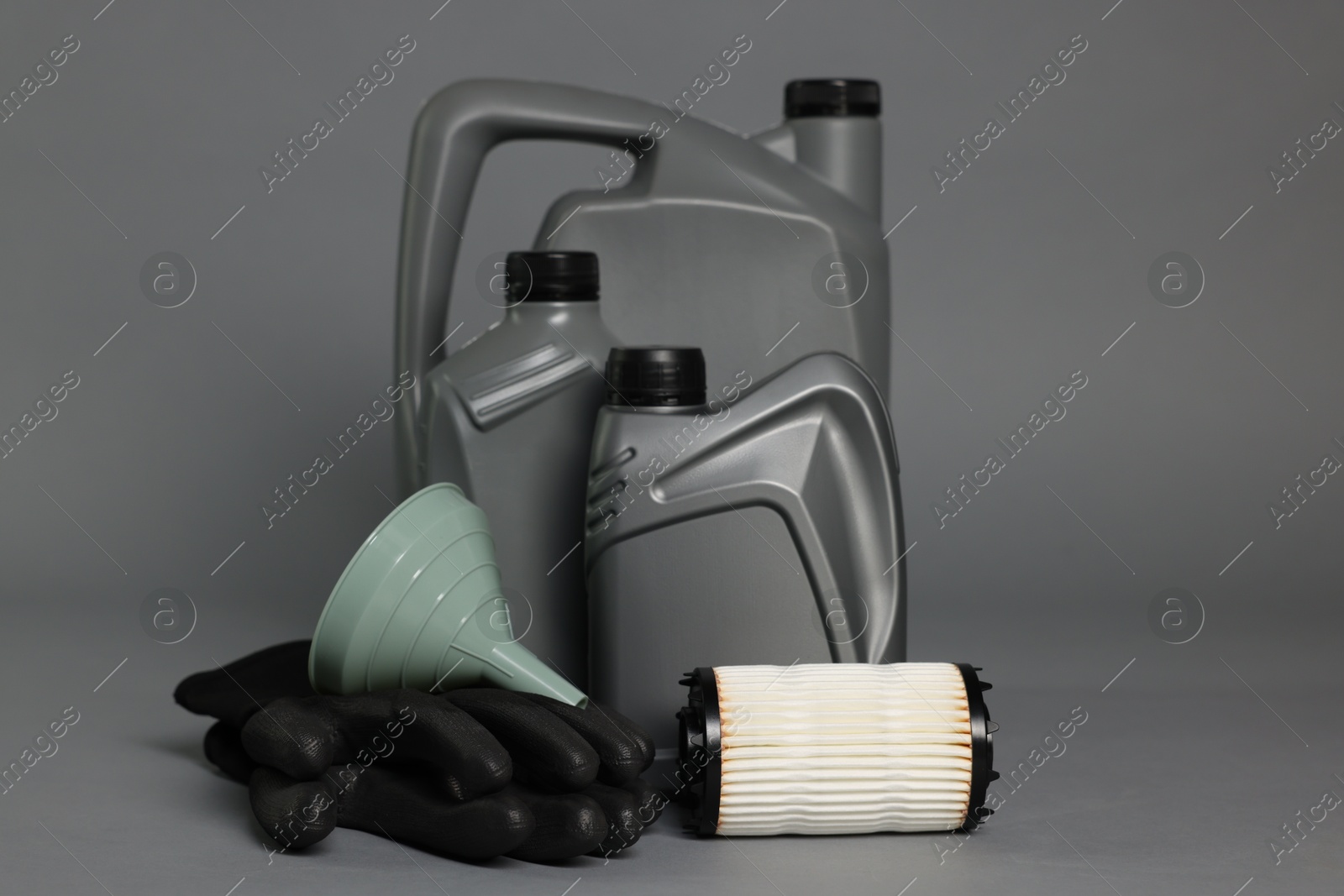 Motor oil in plastic canisters, filter, gloves and funnel on grey background Photo of Motor oil in plastic canisters, filter, gloves and funnel on grey background