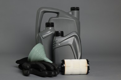 Photo of Motor oil in plastic canisters, filter, gloves and funnel on grey background
