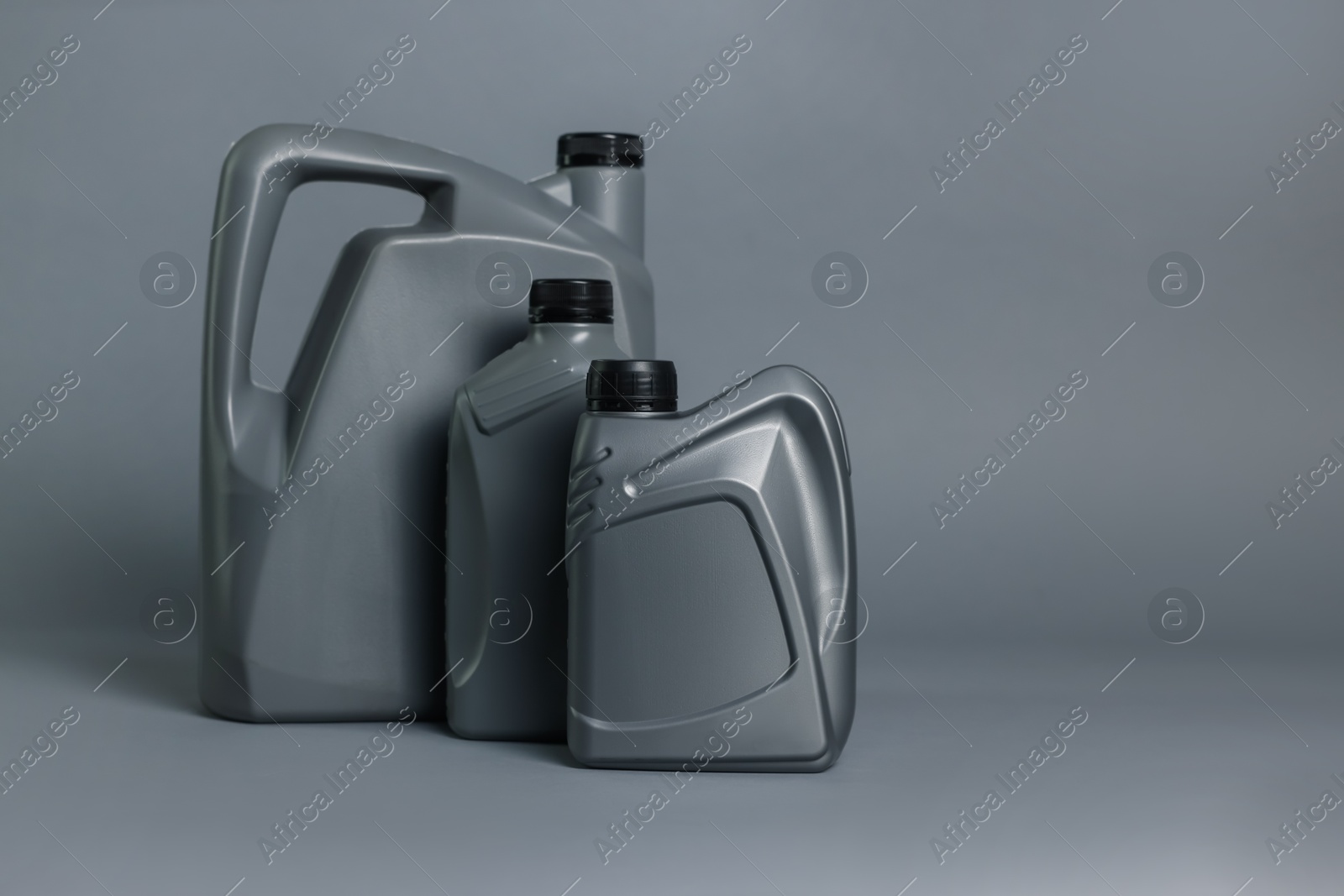Motor oil in plastic canisters on grey background, space for text Photo of Motor oil in plastic canisters on grey background, space for text