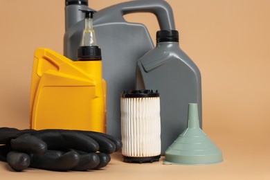 Photo of Motor oil in plastic canisters, filter, gloves and funnel on beige background, closeup