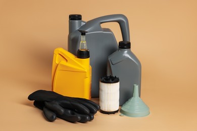 Photo of Motor oil in plastic canisters, filter, gloves and funnel on beige background