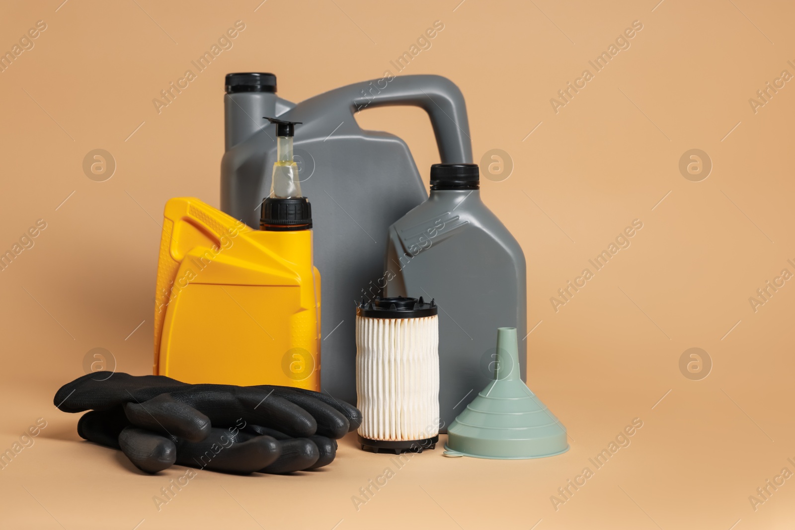 Motor oil in plastic canisters, filter, gloves and funnel on beige background, space for text Photo of Motor oil in plastic canisters, filter, gloves and funnel on beige background, space for text