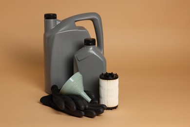 Photo of Motor oil in plastic canisters, filter, gloves and funnel on beige background, space for text