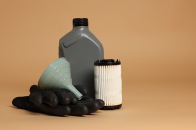 Photo of Motor oil in plastic canister, filter, gloves and funnel on beige background, space for text