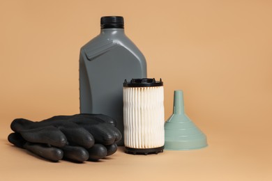 Photo of Motor oil in plastic canister, filter, gloves and funnel on beige background