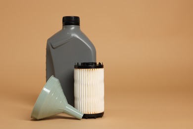 Photo of Motor oil in plastic canister, filter and funnel on beige background, space for text