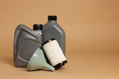 Photo of Motor oil in plastic canisters, filter and funnel on beige background, space for text
