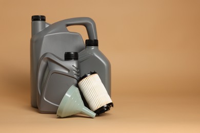 Photo of Motor oil in plastic canisters, filter and funnel on beige background, space for text