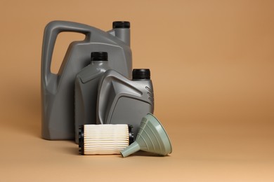 Photo of Motor oil in plastic canisters, filter and funnel on beige background, space for text