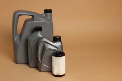 Photo of Motor oil in plastic canisters and filter on beige background, space for text