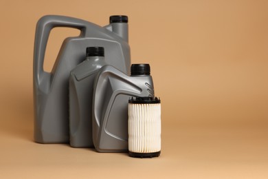 Photo of Motor oil in plastic canisters and filter on beige background, space for text