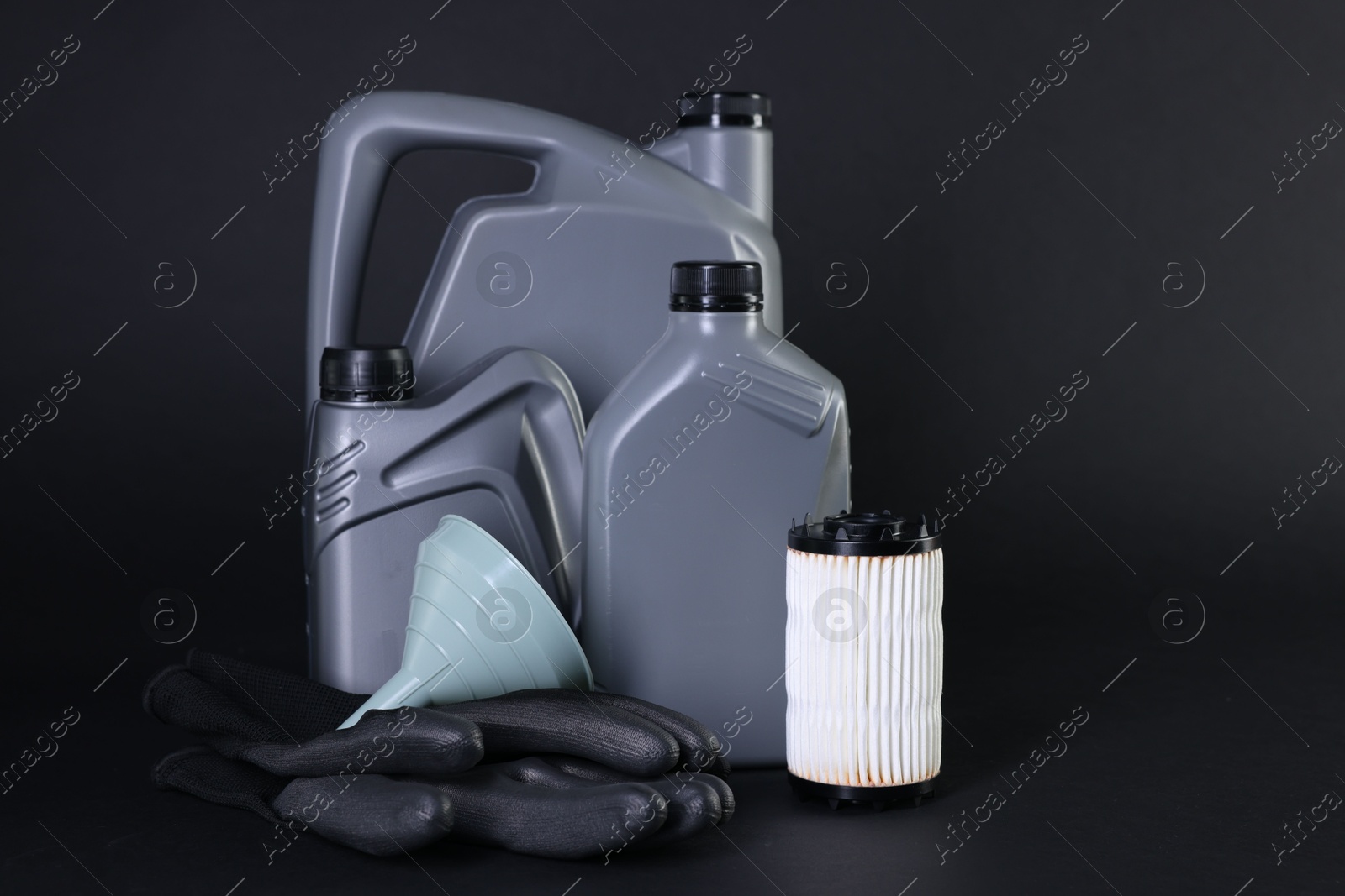 Motor oil in plastic canisters, filter, gloves and funnel on black background Photo of Motor oil in plastic canisters, filter, gloves and funnel on black background