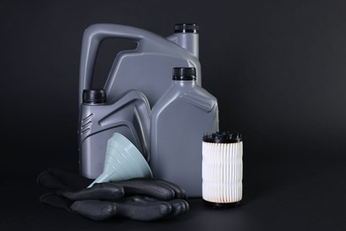 Photo of Motor oil in plastic canisters, filter, gloves and funnel on black background