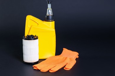 Photo of Motor oil in plastic canister, gloves and filter on dark grey background, space for text