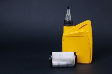 Photo of Motor oil in plastic canister and filter on dark grey background, space for text