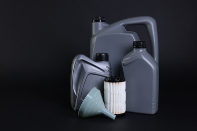 Photo of Motor oil in plastic canisters, filter and funnel on black background, space for text