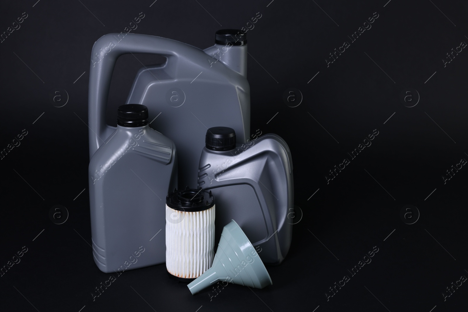 Motor oil in plastic canisters, filter and funnel on black background, space for text Photo of Motor oil in plastic canisters, filter and funnel on black background, space for text