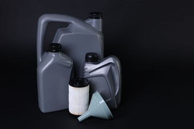 Photo of Motor oil in plastic canisters, filter and funnel on black background, space for text