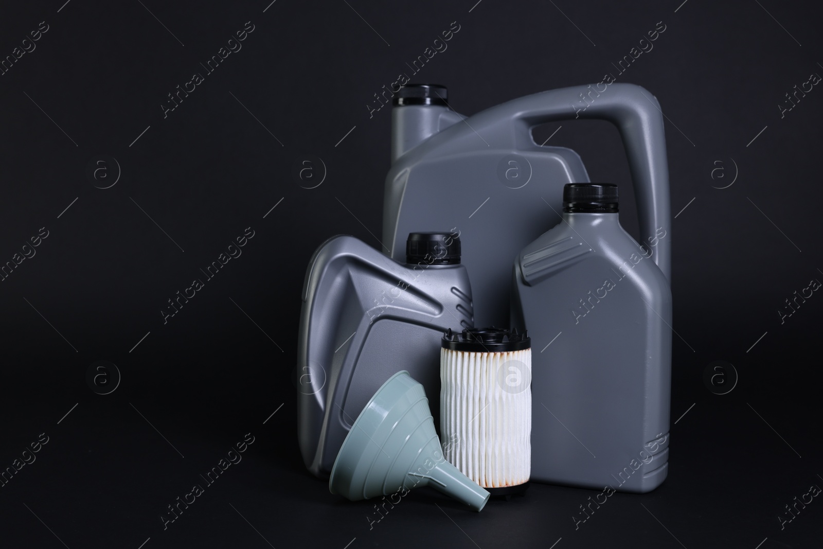 Motor oil in plastic canisters, filter and funnel on black background, space for text Photo of Motor oil in plastic canisters, filter and funnel on black background, space for text