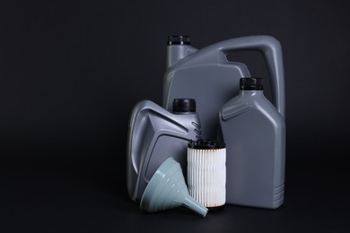 Photo of Motor oil in plastic canisters, filter and funnel on black background, space for text