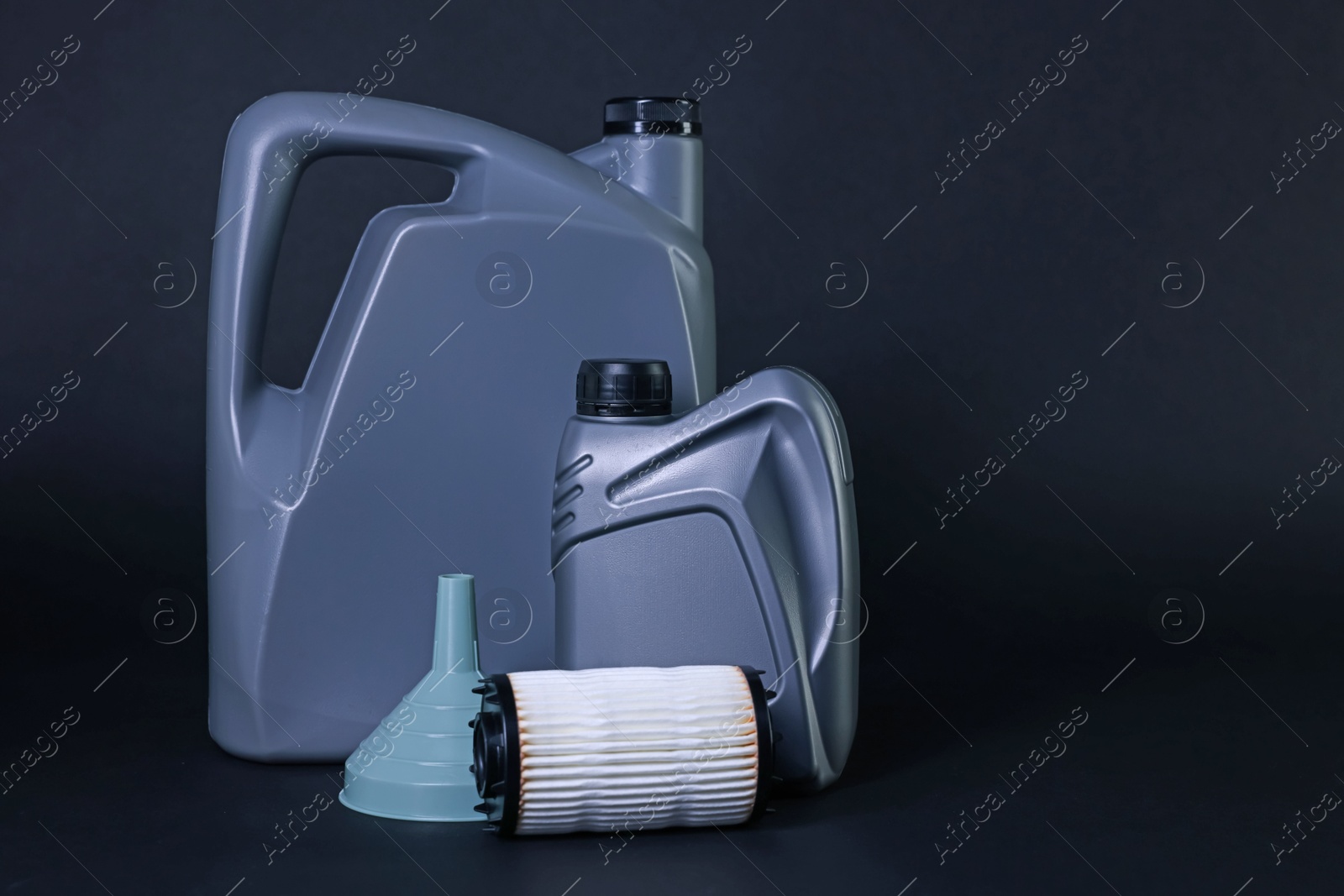 Motor oil in plastic canisters, filter and funnel on dark grey background, space for text Photo of Motor oil in plastic canisters, filter and funnel on dark grey background, space for text