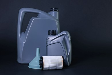 Photo of Motor oil in plastic canisters, filter and funnel on dark grey background, space for text