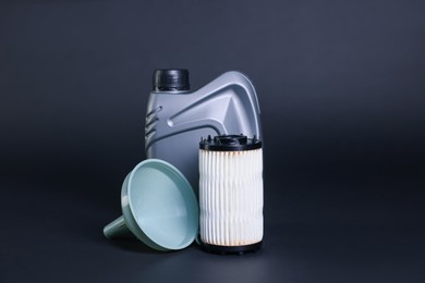 Photo of Motor oil in plastic canister, filter and funnel on dark grey background