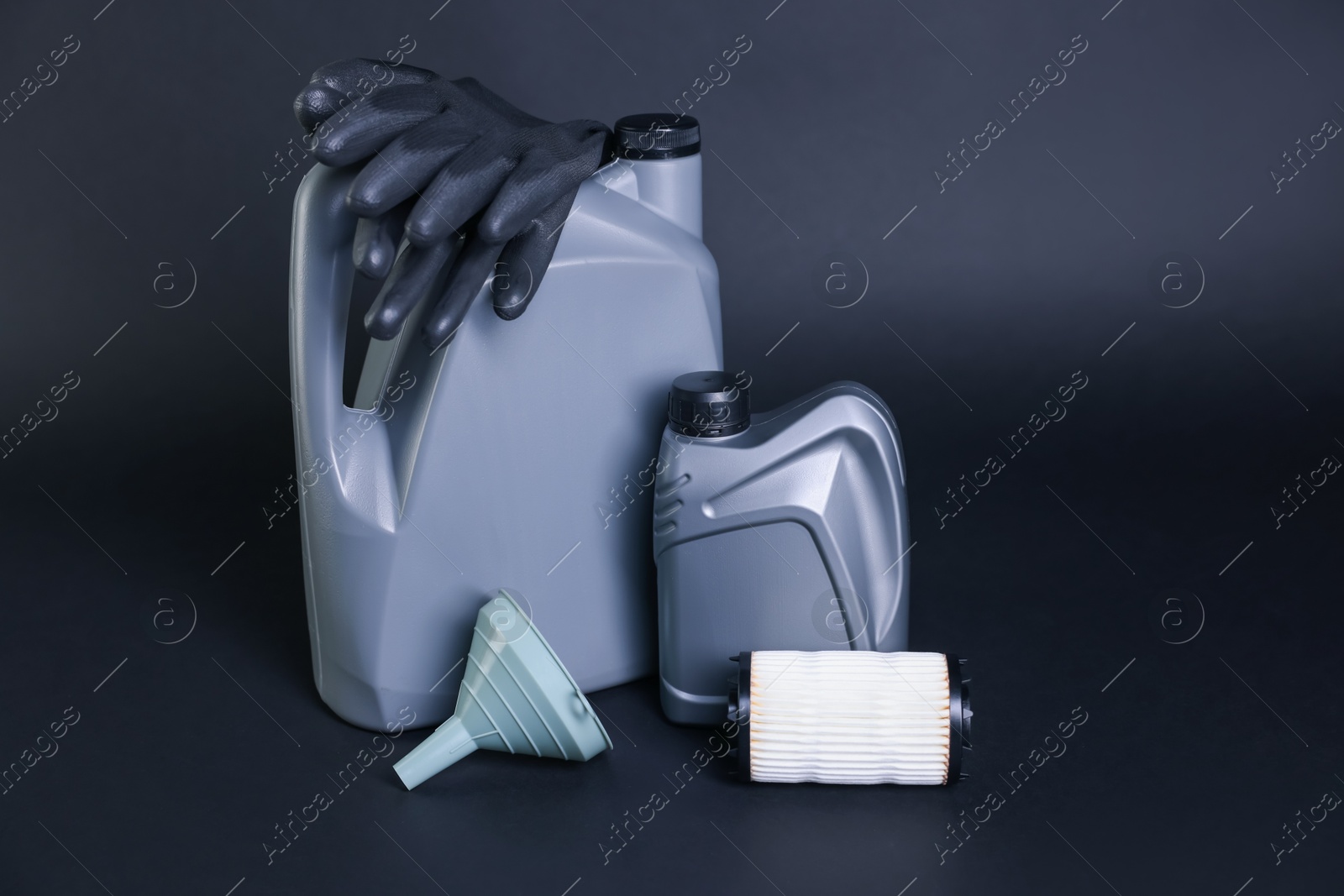 Motor oil in plastic canisters, filter, gloves and funnel on dark grey background Photo of Motor oil in plastic canisters, filter, gloves and funnel on dark grey background
