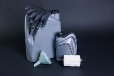 Photo of Motor oil in plastic canisters, filter, gloves and funnel on dark grey background