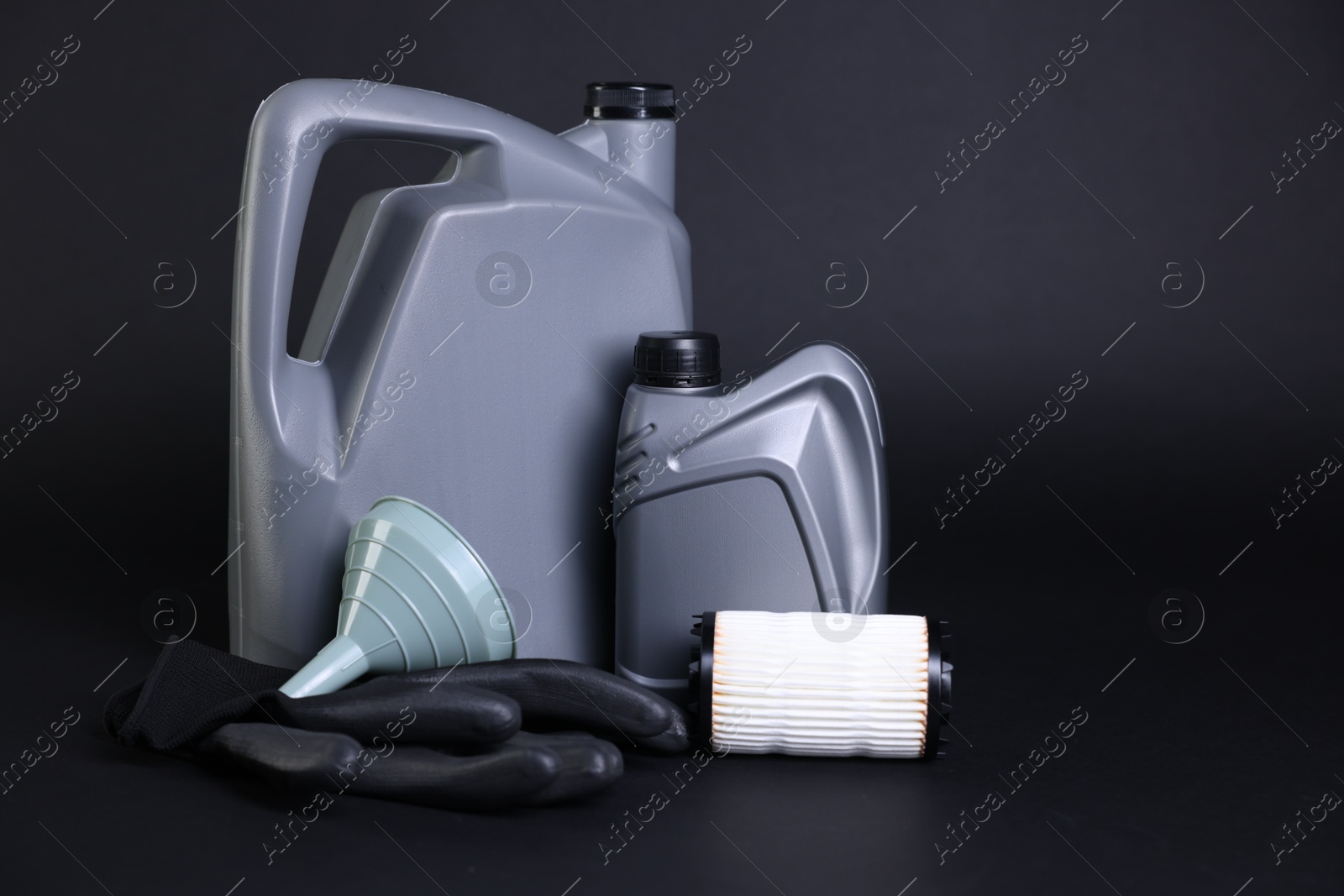 Motor oil in plastic canisters, filter, gloves and funnel on black background, space for text Photo of Motor oil in plastic canisters, filter, gloves and funnel on black background, space for text