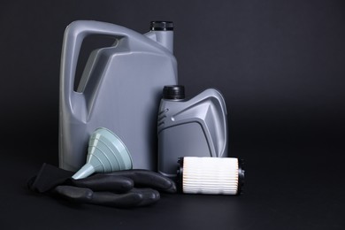 Photo of Motor oil in plastic canisters, filter, gloves and funnel on black background, space for text