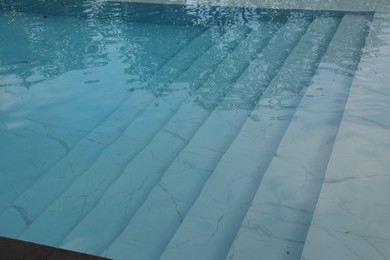Photo of Clear water with ripples and stairs in outdoor swimming pool, closeup