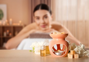 Image of Spa therapy. Woman lying on massage table and aroma lamp in salon, selective focus