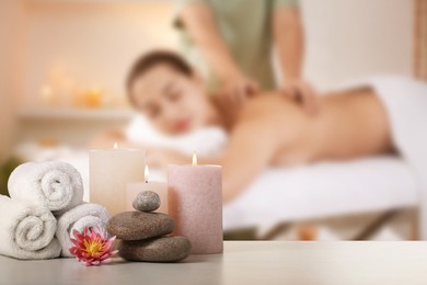 Image of Spa therapy. Woman receiving massage on table and composition with stones, candles and towels in salon, selective focus