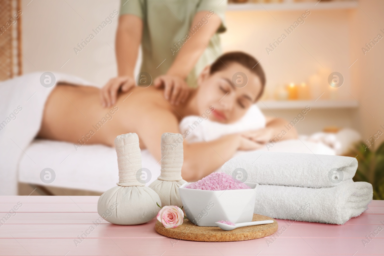 Spa therapy. Woman receiving massage on table and composition with herbal bags, sea salt and towels in salon, selective focus Image of Spa therapy. Woman receiving massage on table and composition with herbal bags, sea salt and towels in salon, selective focus