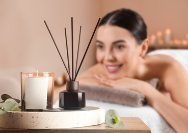 Image of Spa therapy. Woman lying on massage table and composition with aromatic reed air freshener in salon, selective focus