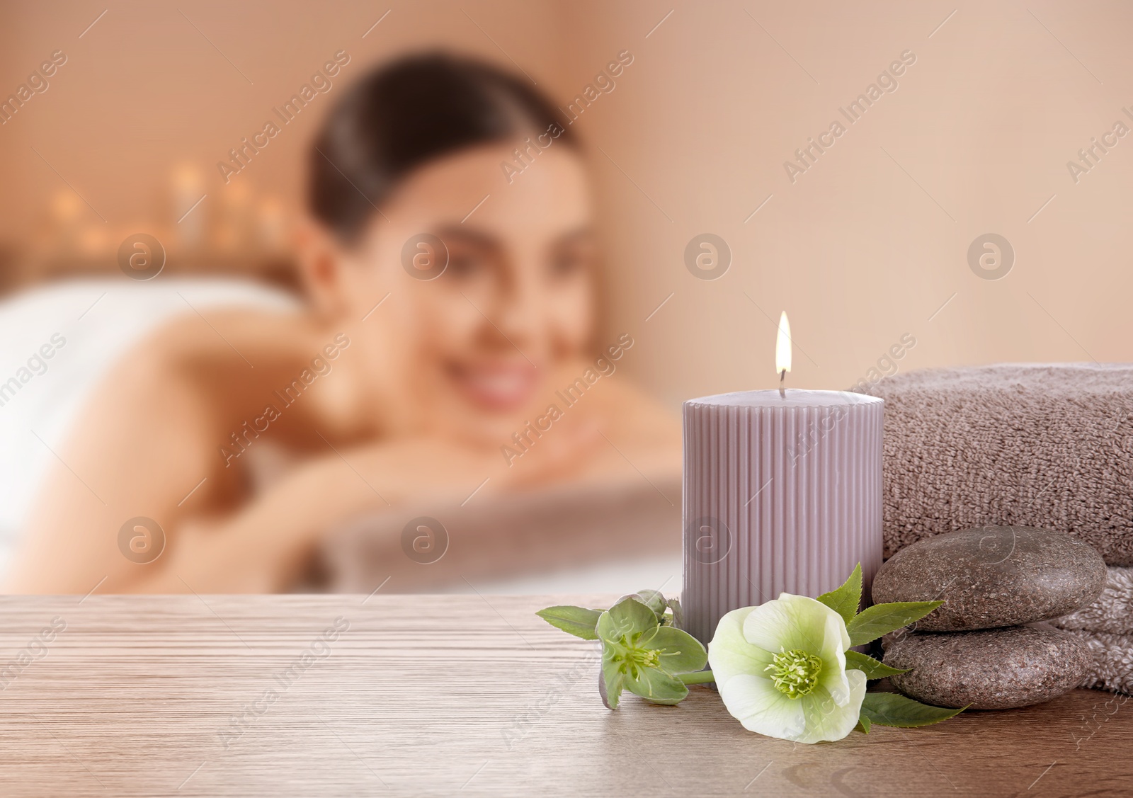 Spa therapy. Woman lying on massage table and composition with candle and stones in salon, selective focus Image of Spa therapy. Woman lying on massage table and composition with candle and stones in salon, selective focus